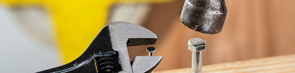 Foto de um martelo batendo em um parafuso e uma chave inglesa rosqueando um prego.